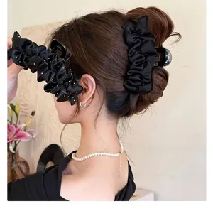 Détail d'une grande pince à cheveux en satin plissé noir portée sur un chignon élégant