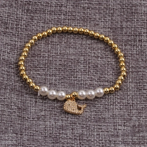 Detail of gold beads and white pearls bracelet featuring a zircon dolphin pendant