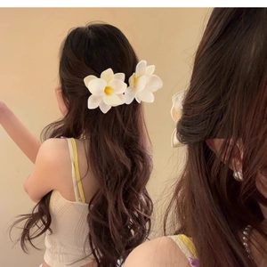 Realistic white plumeria flower hair clip accessory worn on elegant long wavy hair