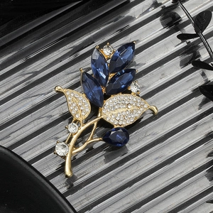Elegant gold leaf brooch with deep blue crystals and rhinestones on a wavy background