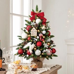Mini lighted desktop Christmas tree with red ornaments and burlap base in cozy room