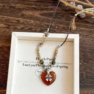 Macro shot of retro heart-shaped ceramic pendant with silver floral metal and woven cord