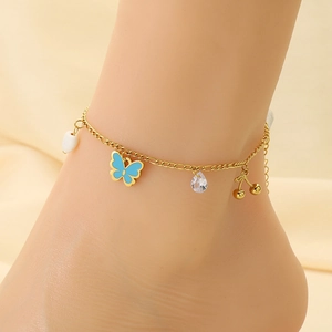 Gold anklet with blue butterfly, cherry, and shell heart charms worn on an ankle