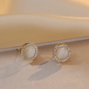 Detailed close-up of golden round cat-eye stone earrings with sparkling zircon halo