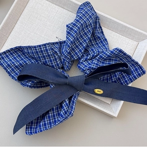 Detailed shot of blue checkered scrunchie with dark blue bow and gold engraved metal charm