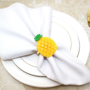 Close-up of a yellow pineapple napkin ring holder on a white napkin over a gold plate