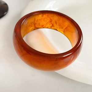 Close-up of amber resin bangle with marbled texture on white ceramic surface