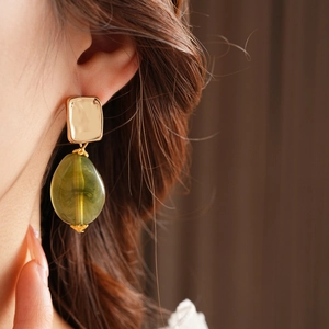 Close-up of golden square stud with a green resin teardrop pendant on female model ear