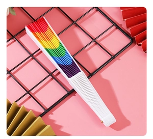 Close-up of a rainbow folding fan with white plastic ribs on a pink background