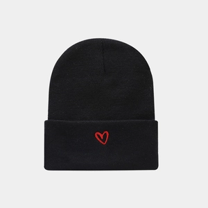 Detail of black knitted beanie featuring a small red embroidered heart on the folded cuff