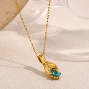 Macro d'un pendentif main plaqué or 18K tenant une pierre bleue sur support bois