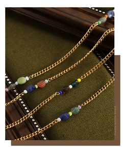 Detail of vintage gold plated necklace with colorful natural stones on green fabric