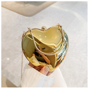 Detail of a gold heart-shaped acrylic clutch bag with a round handle and chain strap
