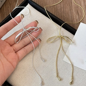 Macro detail of bow-knot necklace with tassels in gold and silver metal finishes