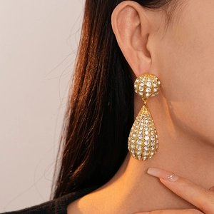 Close-up of a model wearing gold waterdrop earrings with paved diamonds and metallic stripes