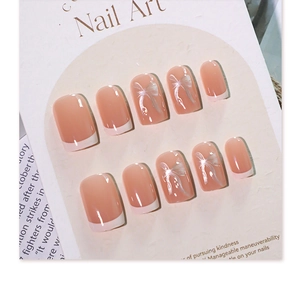 Macro detail of French pale yellow press-on nails with golden bow designs on card