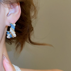 Detail of C-shaped blue denim earrings with pearls and gold metal wrap on a female model