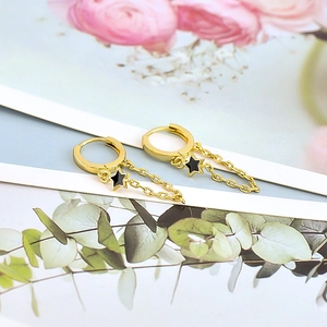 Macro detail of gold star chain earring with black enamel star and flower background