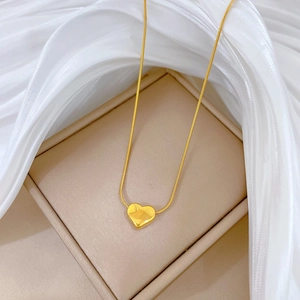 Elegant gold heart pendant necklace featuring a sleek snake chain on white silk background