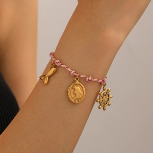 Gros plan d'un bracelet tressé rose et blanc avec des charms dorés sirène et gouvernail