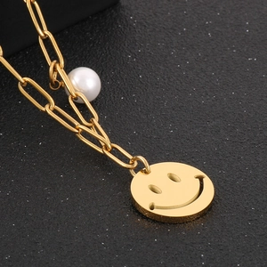 Detailed close-up of golden paperclip necklace with smiley face charm and white pearl