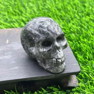 Detailed macro shot of a hand-carved 5cm natural gemstone skull on a dark wooden base
