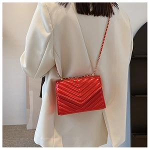 Detail of red patent leather crossbody bag with V-shaped quilting and gold chain strap