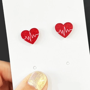 Detail of red heart earrings with white heartbeat lines and glitter finish on card