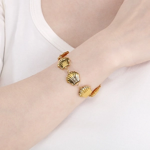 Detailed view of a gold-plated shell bracelet worn on the wrist with scalloped links