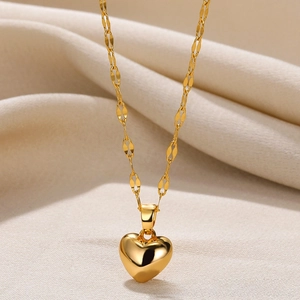 Close-up of 18k gold heart pendant on textured olive link chain over beige fabric