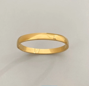 Close-up of polished gold-plated stainless steel bangle with a minimalist hinge closure