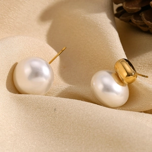 Detail view of 18K gold plated stainless steel pearl earrings on beige fabric background