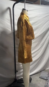 Detail van gouden satijnen tweedelige set met geplooide textuur en shirt met lange mouwen