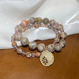 Macro detail of double-layer beaded bracelet with stone beads and a gold tree pendant