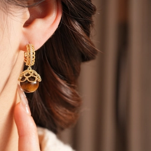 Detail of gold plated hollow flower earrings with brown tiger eye stones and zircon accents