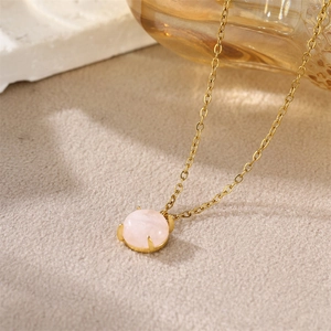 Minimalist gold necklace with a pink round stone pendant on a beige velvet texture