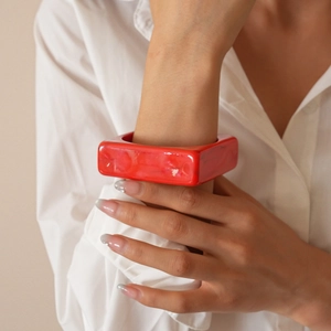 Macro detail of red chunky square acrylic bangle on wrist with polished finish