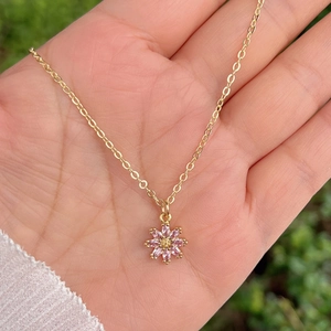 Gros plan d'un collier pendentif tournesol doré avec pétales en zircon rose dans la main
