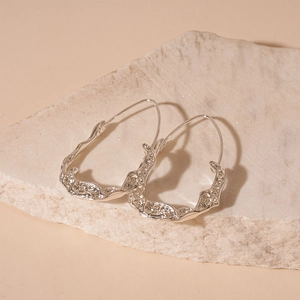 Detailed shot of silver liquid metal earrings with irregular texture on a stone prop