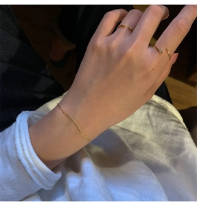 Detail view of gold chain bracelet with embedded crystals and minimalist open rings on model