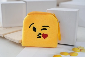 Close-up of yellow plush emoji coin purse with embroidered winking face and red heart detail