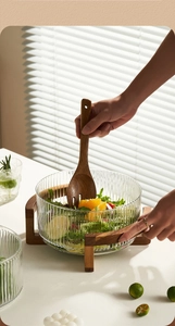 Detailed view of fluted glass salad bowl with wooden stand and matching serving spoon