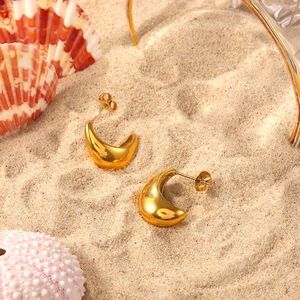Close-up of chunky gold hoop earrings with shell and glassware on beach sand