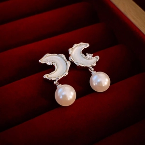 Detail of moon-shaped earrings with zircon and pearl on dark red velvet box