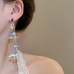 Macro detail of long tassel earrings with blue crystals and white petals on model
