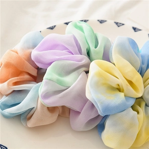 Macro detail of colorful tie-dye chiffon scrunchies with soft pleated texture in a white dish