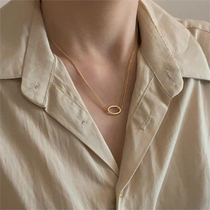 Close-up of a layered gold oval pendant necklace worn on a beige linen shirt