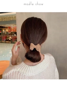 Detail view of plush bow hair tie in beige velvet material styled on a low ponytail