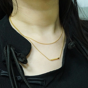 Minimalist double-layered gold necklace with bar pendant shown on neck over black outfit