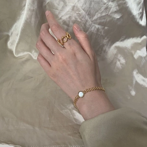 Detail of gold chain bracelet with round white shell inlay and LOVE letter ring on silk